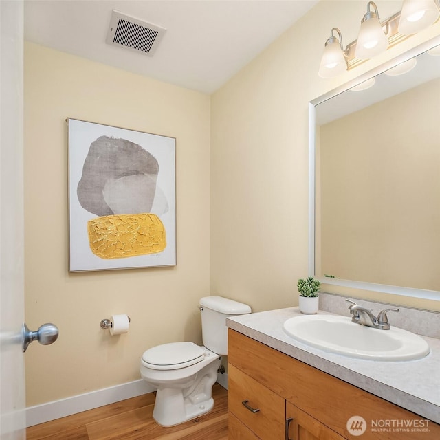 half bath with visible vents, toilet, wood finished floors, baseboards, and vanity