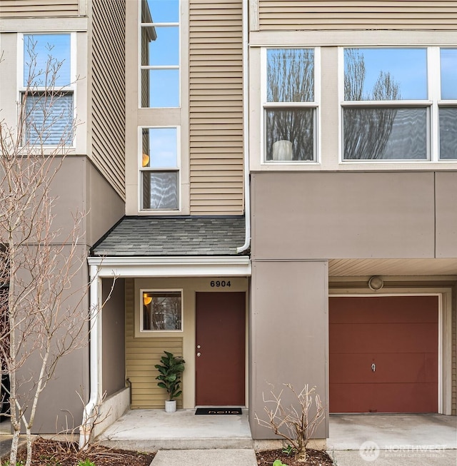 view of exterior entry featuring stucco siding, a shingled roof, and a garage