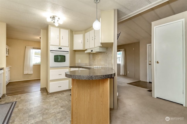 kitchen featuring pendant lighting, white cabinetry, decorative backsplash, light colored carpet, and oven