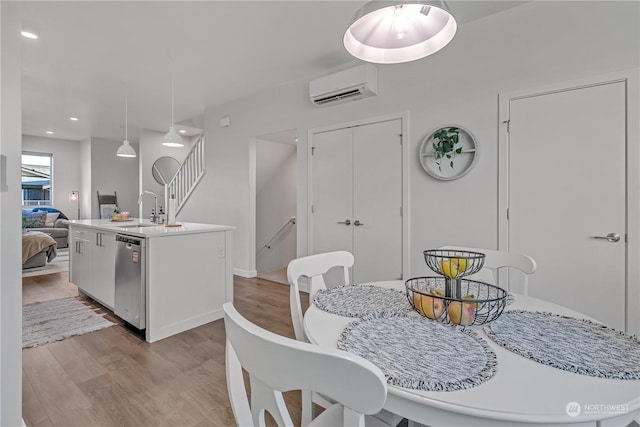 dining space with a wall mounted air conditioner, sink, and light wood-type flooring