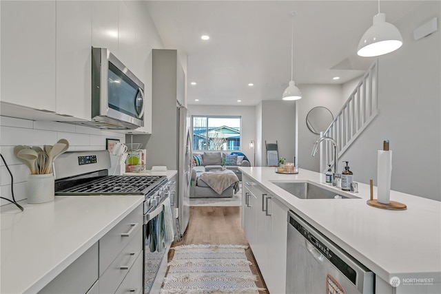 kitchen with sink, light hardwood / wood-style flooring, appliances with stainless steel finishes, pendant lighting, and backsplash