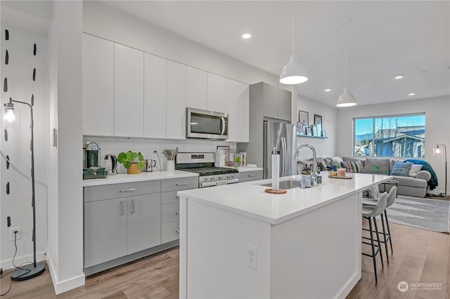 kitchen featuring sink, hanging light fixtures, appliances with stainless steel finishes, a kitchen breakfast bar, and an island with sink