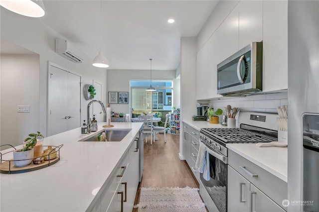 kitchen with sink, stainless steel appliances, white cabinets, decorative light fixtures, and an AC wall unit