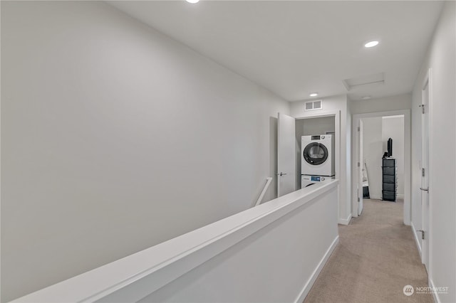 hallway featuring stacked washer / drying machine and light colored carpet