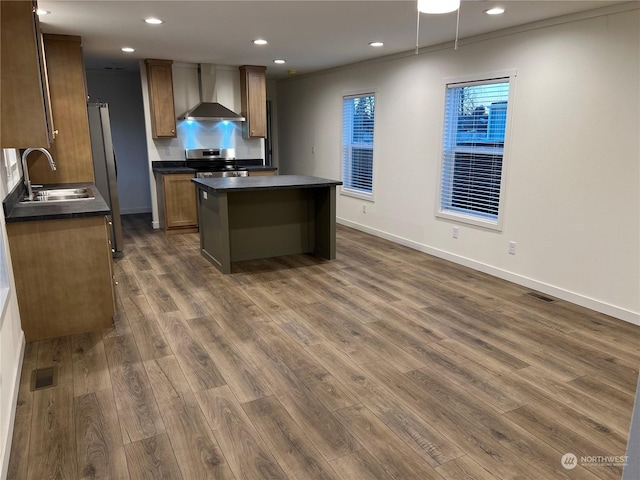 kitchen with wall chimney range hood, sink, stainless steel range with electric stovetop, a kitchen island, and dark hardwood / wood-style flooring