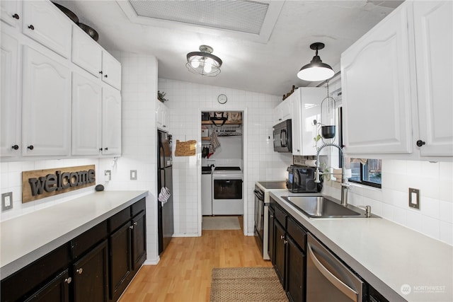 kitchen with sink, white cabinets, washing machine and clothes dryer, light hardwood / wood-style floors, and black appliances