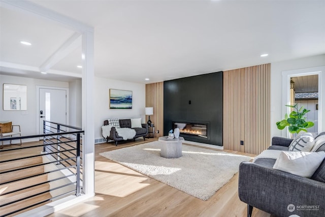 living room with beamed ceiling, a large fireplace, and light wood-type flooring