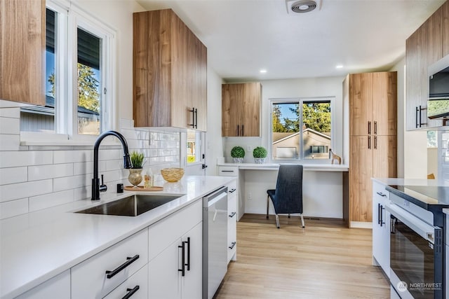 kitchen with tasteful backsplash, sink, white cabinets, stainless steel dishwasher, and light hardwood / wood-style flooring