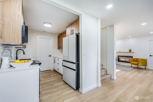 kitchen featuring white refrigerator, backsplash, sink, and light wood-type flooring