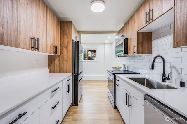 kitchen with appliances with stainless steel finishes, sink, white cabinets, decorative backsplash, and light hardwood / wood-style flooring