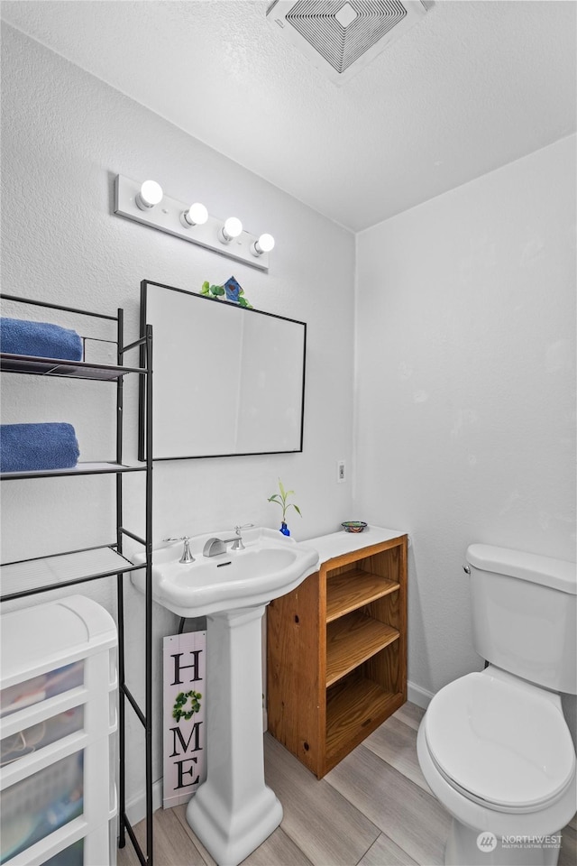 bathroom featuring wood-type flooring, a textured ceiling, and toilet