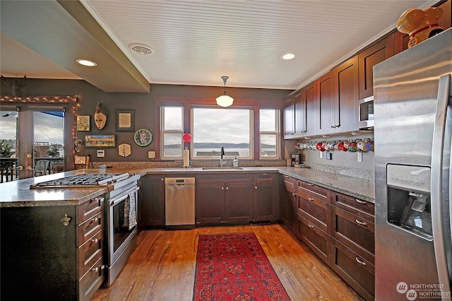 kitchen featuring light wood finished floors, appliances with stainless steel finishes, hanging light fixtures, light stone countertops, and a sink