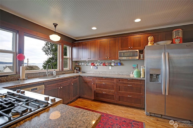 kitchen with stainless steel appliances, a sink, light wood-type flooring, dark stone countertops, and decorative light fixtures