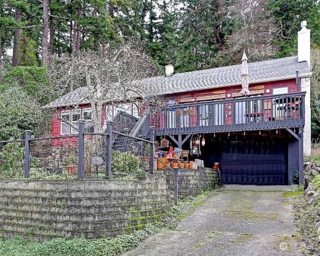 view of front facade with aphalt driveway, a chimney, and a wooden deck