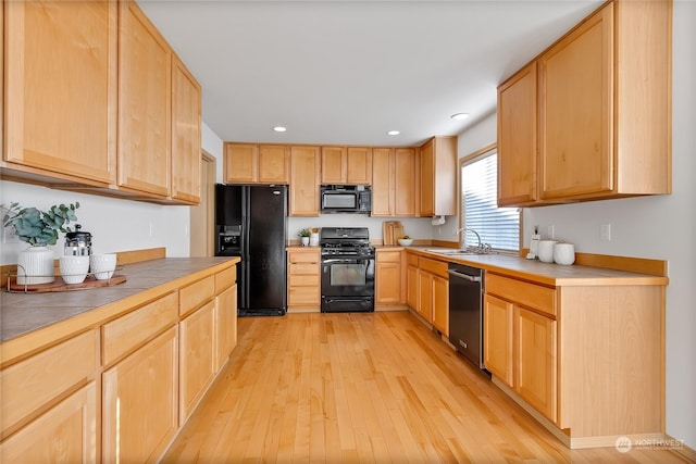 kitchen featuring light brown cabinets, light wood-style flooring, a sink, tile counters, and black appliances