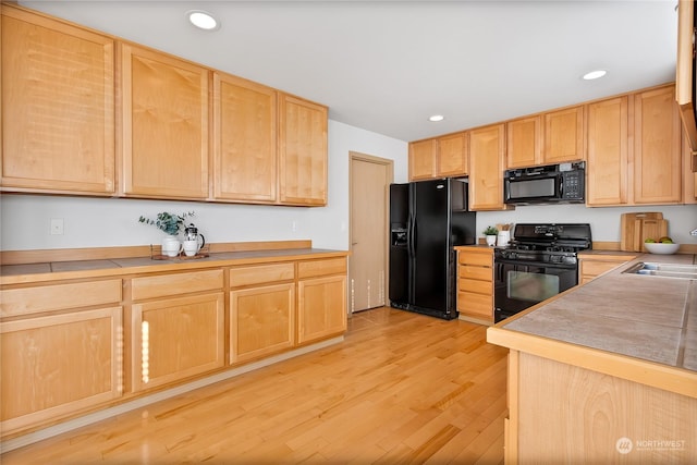 kitchen with light wood finished floors, black appliances, light brown cabinets, a sink, and recessed lighting