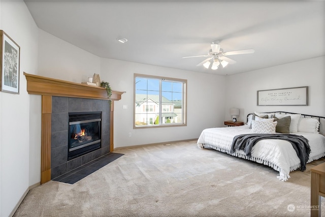 bedroom with ceiling fan, a tiled fireplace, baseboards, and carpet flooring