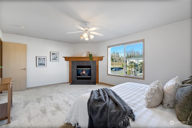 bedroom featuring a tile fireplace, light colored carpet, ceiling fan, and baseboards