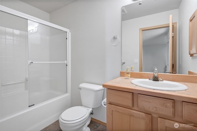 full bathroom featuring toilet, baseboards, bath / shower combo with glass door, and vanity