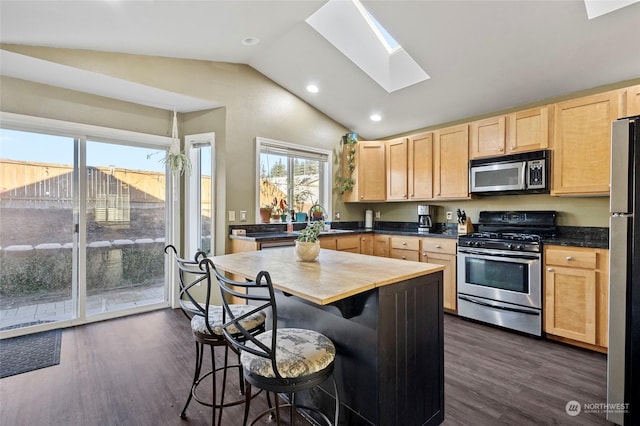 kitchen featuring appliances with stainless steel finishes, dark hardwood / wood-style floors, vaulted ceiling with skylight, a kitchen bar, and light brown cabinets