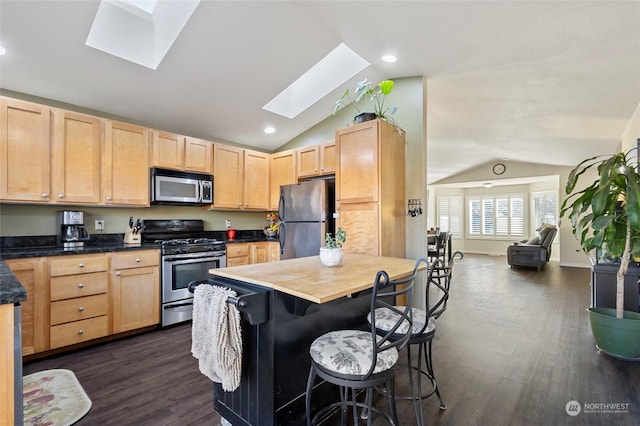 kitchen with vaulted ceiling with skylight, light brown cabinetry, a breakfast bar area, stainless steel appliances, and dark wood-type flooring