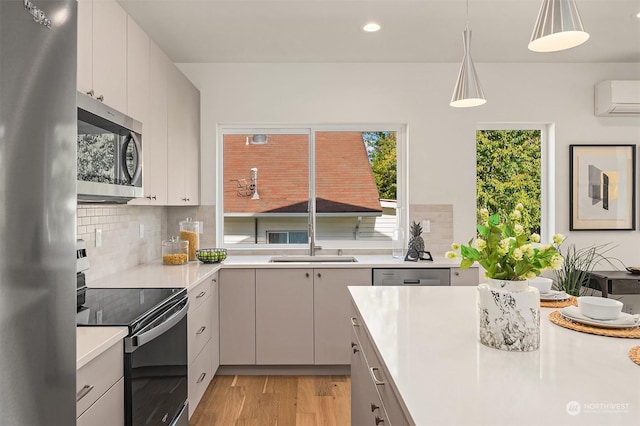 kitchen featuring tasteful backsplash, a wall mounted air conditioner, decorative light fixtures, stainless steel appliances, and light hardwood / wood-style floors