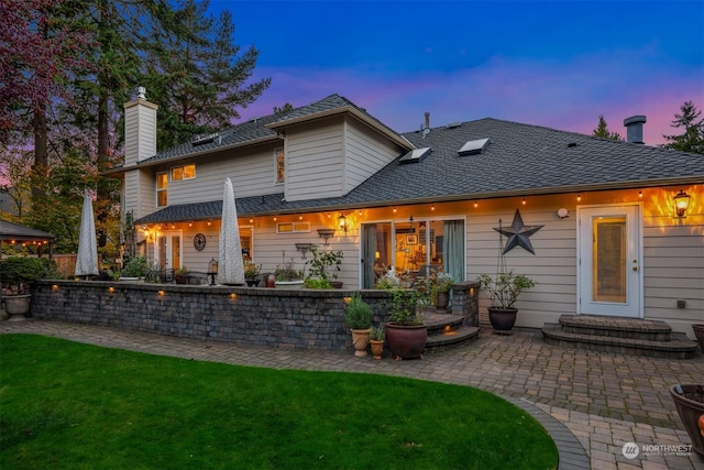 back house at dusk featuring a patio and a yard