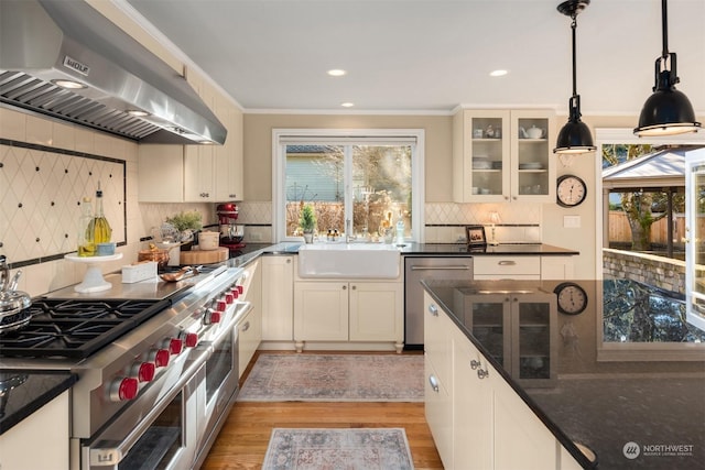 kitchen featuring decorative light fixtures, ventilation hood, ornamental molding, stainless steel appliances, and light hardwood / wood-style flooring