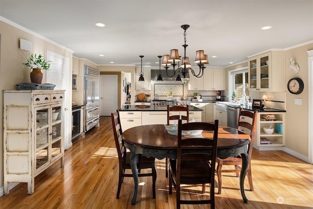 dining space with an inviting chandelier, crown molding, beverage cooler, and light wood-type flooring