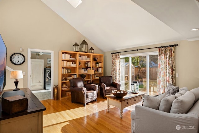 living room featuring washer / clothes dryer, hardwood / wood-style flooring, high vaulted ceiling, and a skylight