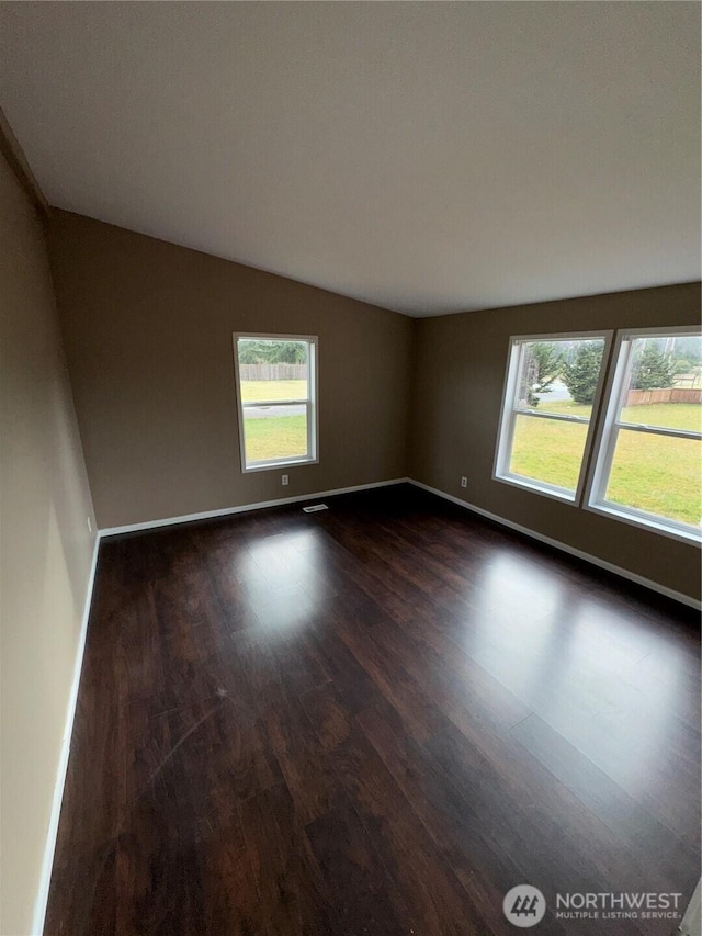 unfurnished room with dark wood-style floors, vaulted ceiling, and baseboards