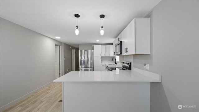 kitchen featuring appliances with stainless steel finishes, white cabinets, hanging light fixtures, kitchen peninsula, and light wood-type flooring