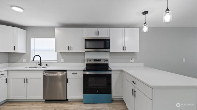 kitchen with sink, stainless steel appliances, white cabinets, decorative light fixtures, and light wood-type flooring