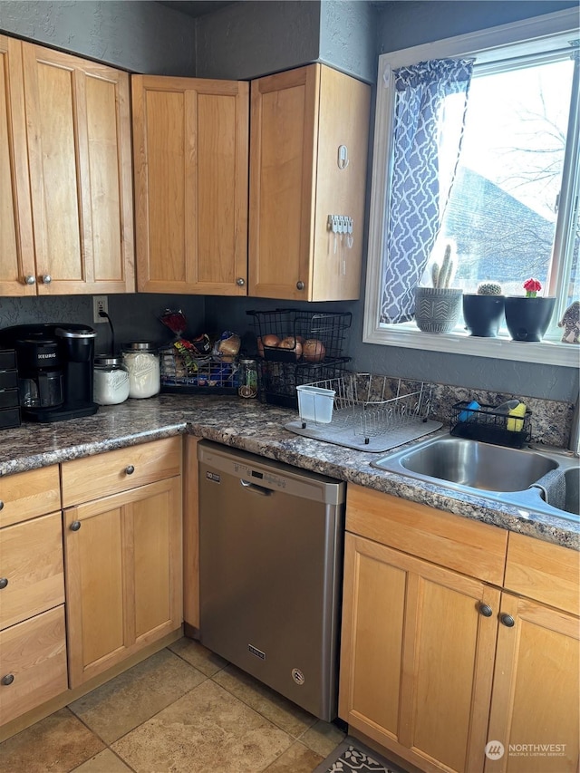 kitchen featuring dark countertops, light brown cabinets, dishwasher, and a sink