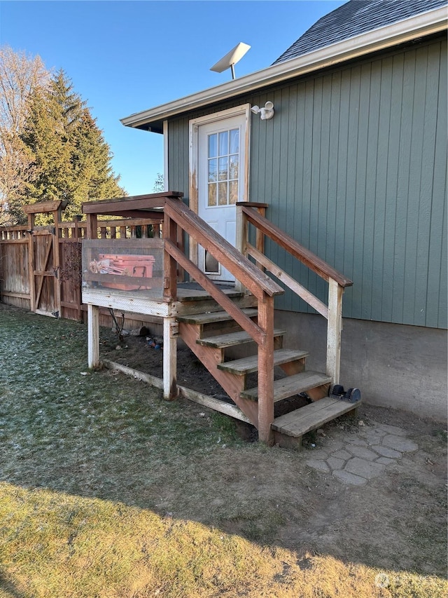 doorway to property featuring a yard, roof with shingles, fence, and a wooden deck