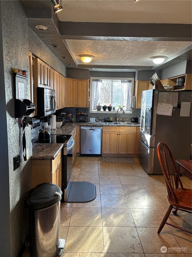 kitchen with dark countertops, appliances with stainless steel finishes, light tile patterned flooring, a sink, and a textured ceiling