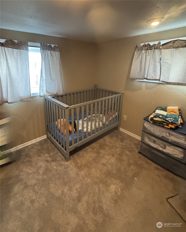 bedroom featuring a crib, a textured ceiling, baseboards, and carpet flooring