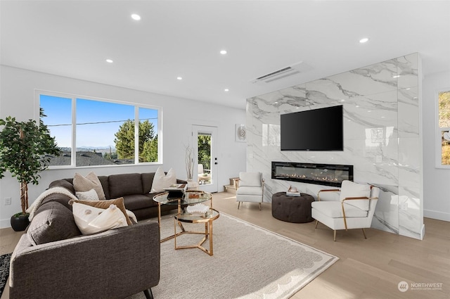 living room with a high end fireplace, light hardwood / wood-style floors, and a wealth of natural light