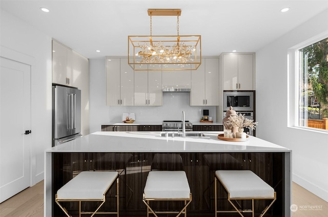 kitchen featuring white cabinets, a kitchen bar, hanging light fixtures, light hardwood / wood-style floors, and stainless steel appliances