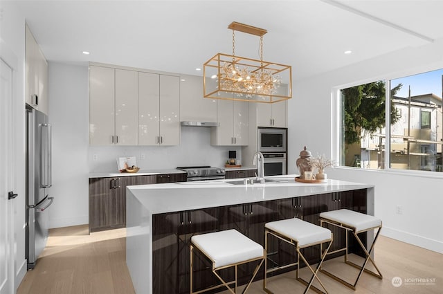 kitchen featuring a kitchen island with sink, a kitchen breakfast bar, stainless steel appliances, white cabinets, and decorative light fixtures