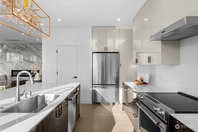 kitchen with sink, appliances with stainless steel finishes, white cabinetry, hanging light fixtures, and wall chimney exhaust hood