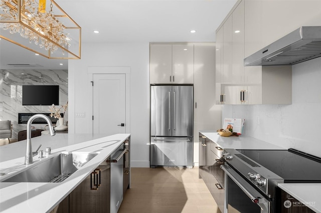 kitchen featuring sink, white cabinetry, hanging light fixtures, stainless steel appliances, and exhaust hood