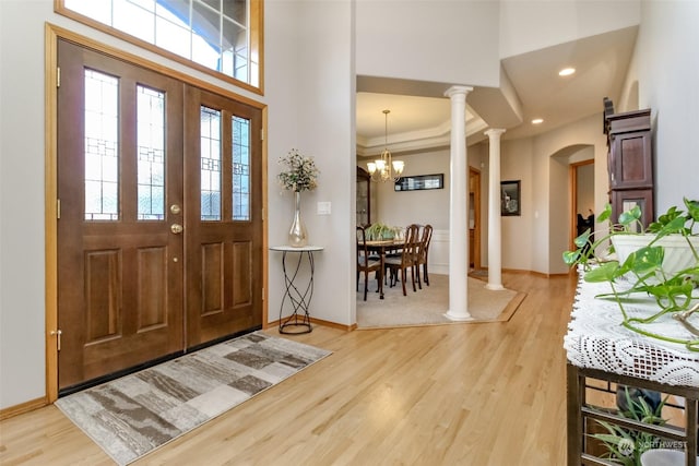 entrance foyer featuring a towering ceiling, decorative columns, hardwood / wood-style flooring, ornamental molding, and a notable chandelier