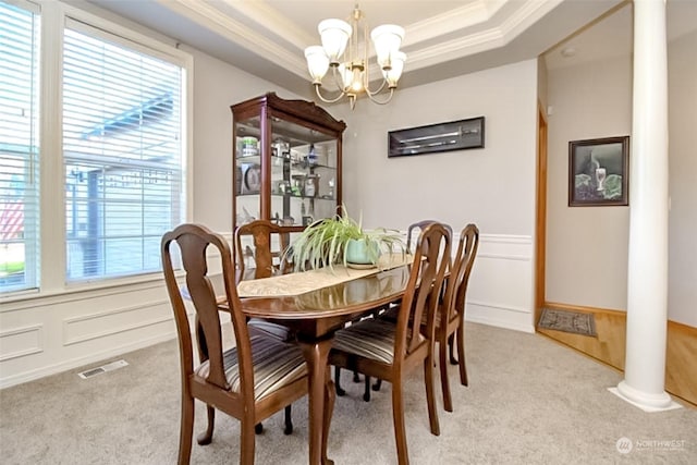 carpeted dining room with an inviting chandelier, crown molding, a raised ceiling, and ornate columns