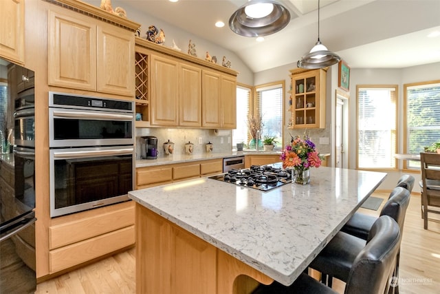 kitchen with stainless steel appliances, a kitchen bar, light brown cabinetry, and light stone counters