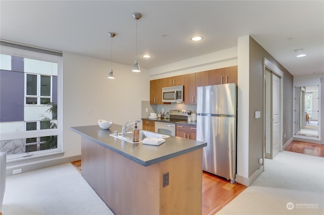 kitchen with pendant lighting, sink, appliances with stainless steel finishes, a kitchen island with sink, and light wood-type flooring