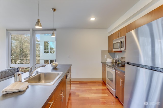 kitchen with appliances with stainless steel finishes, sink, light wood-type flooring, and decorative light fixtures