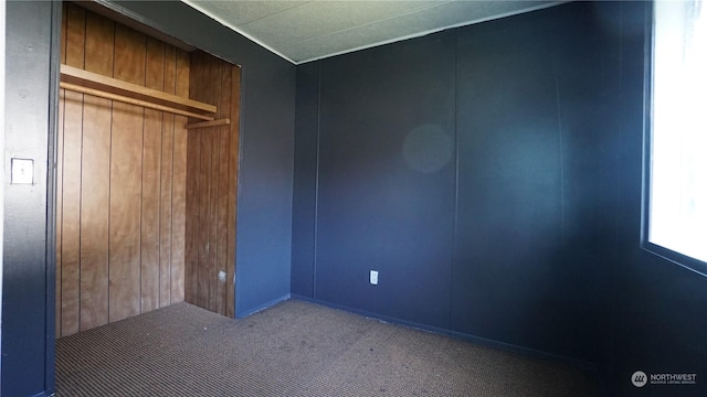 unfurnished bedroom with wooden walls, a closet, and carpet