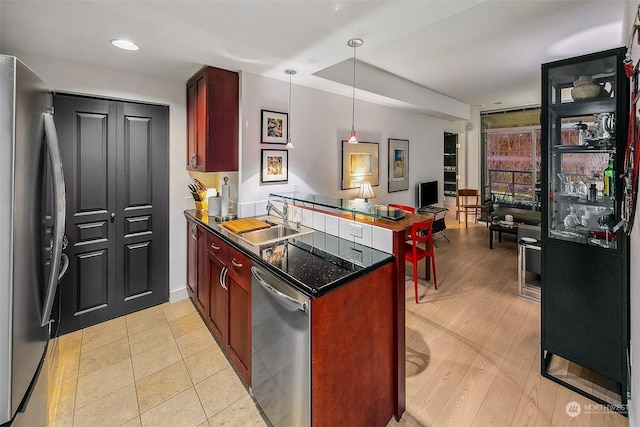 kitchen with pendant lighting, sink, kitchen peninsula, stainless steel appliances, and light wood-type flooring