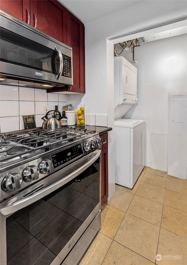 kitchen featuring stacked washing maching and dryer, light tile patterned flooring, decorative backsplash, and appliances with stainless steel finishes